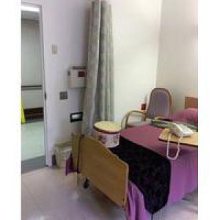 A hospital room with a bed, chair, and medical equipment.