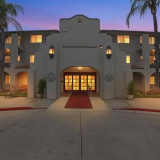 A beautifully illuminated hotel entrance at dusk with palm trees lining the driveway.