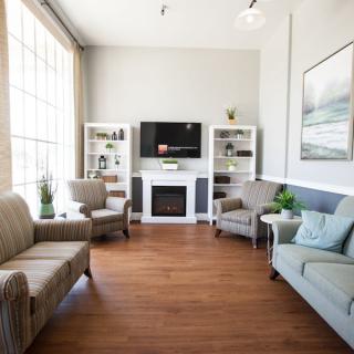 A cozy living room featuring comfortable seating, a television above a fireplace, and bookshelves with decorative items.