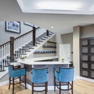 A modern home bar with blue chairs and a stylish staircase.