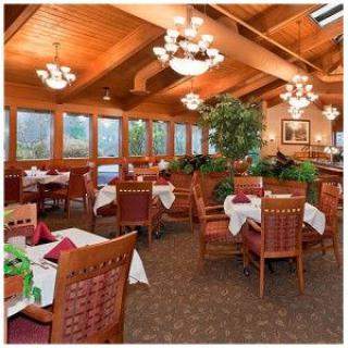 A cozy restaurant dining area with wooden ceilings, elegantly set tables, and large windows providing natural light.