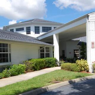 A well-maintained building with a covered entrance, surrounded by lush greenery under a partly cloudy sky.