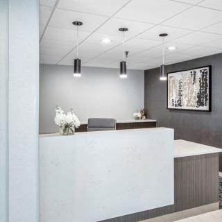A modern and minimalist office reception area with a sleek desk, pendant lighting, and decorative artwork.