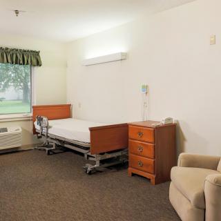 A minimalist hospital room with a single bed, dresser, and chair.
