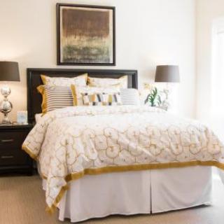 A cozy bedroom featuring a well-made bed with patterned bedding, flanked by nightstands with matching lamps and decorative pillows, beneath a piece of artwork.