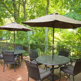 A peaceful outdoor patio area with tables, chairs, and umbrellas surrounded by lush greenery.