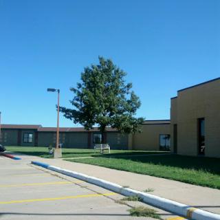 A view of a school building under a clear blue sky, featuring a tree and grassy area.