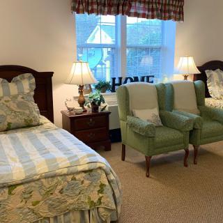 A cozy bedroom with two beds, green armchairs, and warm lighting.