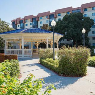 A well-maintained gazebo surrounded by lush landscaping in front of a multi-story apartment building.