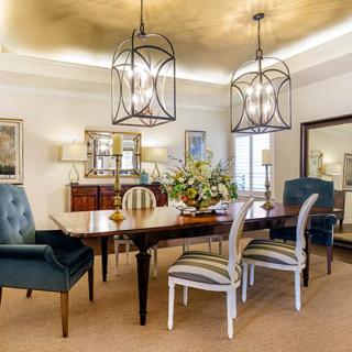 A well-decorated dining room featuring a large wooden table surrounded by various chairs, with elegant chandeliers hanging from the ceiling.