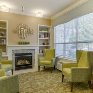 A cozy living room with green chairs, a fireplace, and large bookshelves.