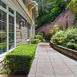 A beautifully landscaped pathway alongside a house with lush greenery and well-maintained shrubs.