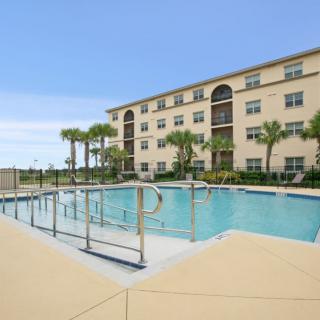 Outdoor swimming pool in front of an apartment building with palm trees on a sunny day.
