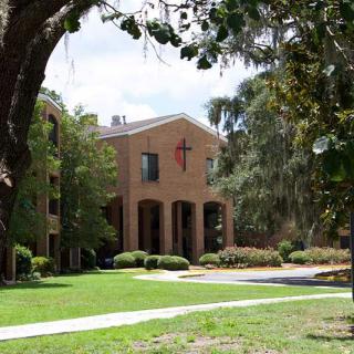 A brick building with a cross on the facade surrounded by trees and grass.