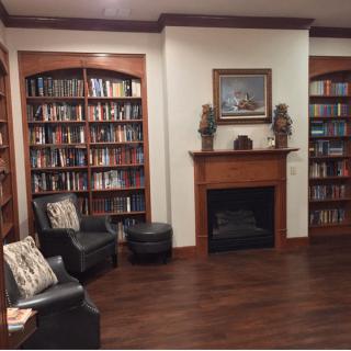 A cozy library room with wooden bookshelves, a fireplace, and comfortable seating.