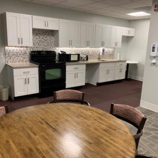 A modern kitchen area in an office, featuring a dining table and various appliances.