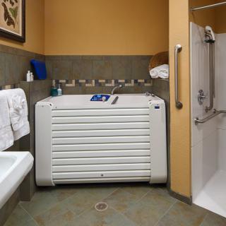 An accessible bathroom featuring a specialized bathtub and shower with handrails.