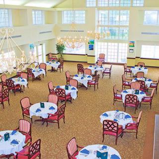 An elegant dining room with well-arranged tables and chairs, featuring chandeliers and decorative table settings.