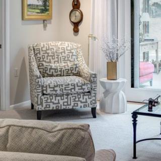 A modern living room with a patterned armchair, a side table with a vase, and decorative elements including artwork and a wall clock.