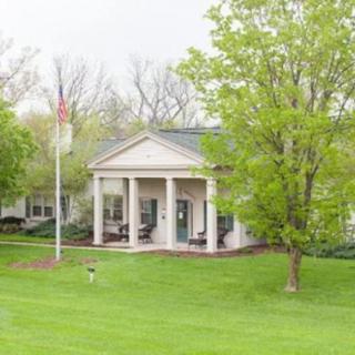A white building with columns surrounded by trees and a manicured lawn.