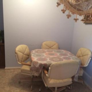 A dining area with a round table and four cushioned chairs, set against a light blue wall.