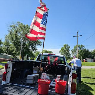 A pickup truck displays an American flag in its bed, surrounded by red buckets and set against a clear blue sky.