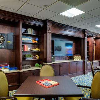 A cozy game room featuring a dartboard, television, and ample seating with wooden cabinetry and decor.