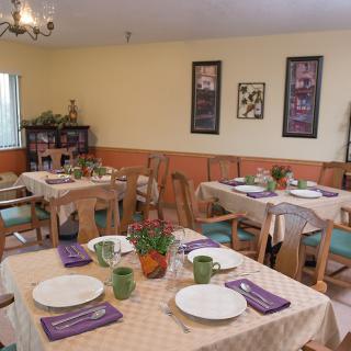 A cozy dining room with neatly arranged tables and chairs, featuring place settings and decorative accents.