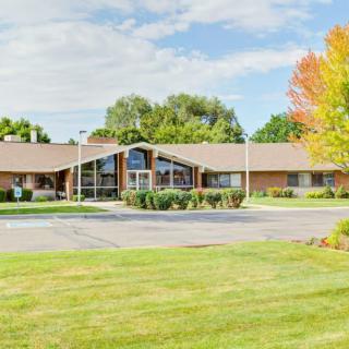 A single-story building surrounded by a well-maintained lawn and trees with autumn foliage under a partly cloudy sky.