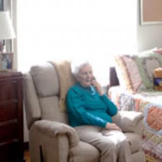 An elderly person sitting in an armchair and talking on the phone in a cozy living room.