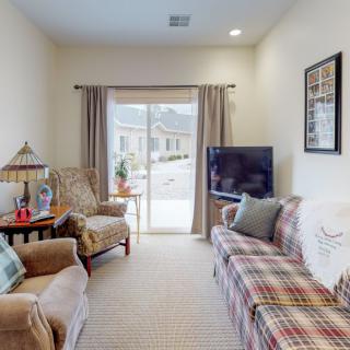 A cozy living room with comfortable seating and a television, featuring a large window with curtains.