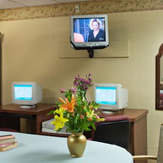 A cozy office space featuring two computers, a television mounted on the wall, and a colorful flower vase.