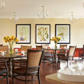 A cozy dining room with elegant decor, featuring several tables and chairs, vases of sunflowers, and framed artwork on the walls.