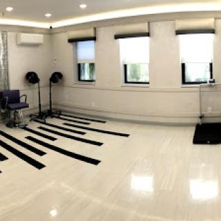 An empty dance studio featuring a polished wooden floor, large windows allowing natural light, and marked areas on the floor.