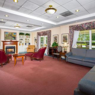 A cozy living room with red carpet, comfortable seating, a fireplace, and large windows.