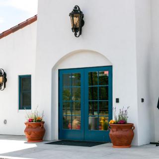 A building entrance featuring a blue door, flanked by potted plants and decorative lanterns on white walls.