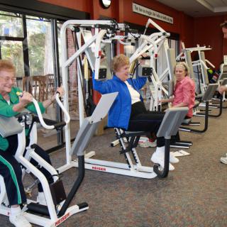 Elderly individuals exercising on gym equipment.