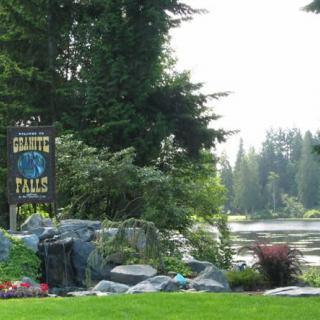 A scenic view of a park with a sign beside a peaceful lake surrounded by trees.