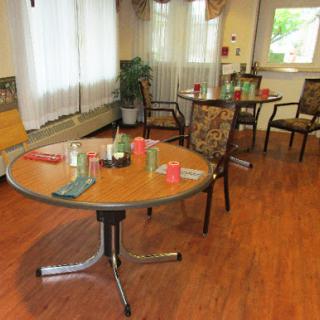 A cozy community dining area featuring several tables and chairs, with natural light streaming in through the windows.