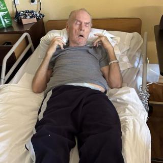An elderly man resting in a hospital bed in a medical setting.