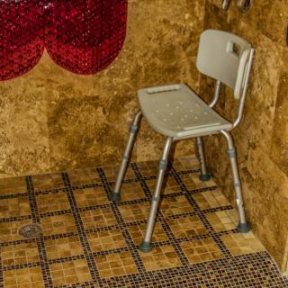 A white chair is placed in a bathroom with mosaic tiled walls and floor.