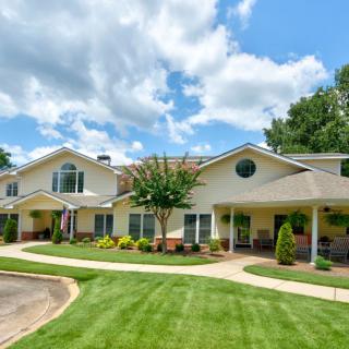 A large residential house with a manicured lawn and lush landscaping under a cloudy blue sky.