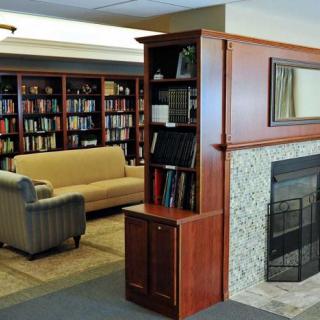 A cozy library with bookshelves, a seating area, and a fireplace.