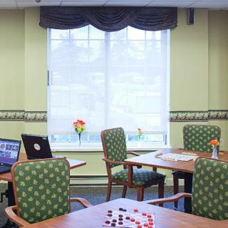 A cozy lounge area with tables, chairs, laptops, and a board game set near a large window.