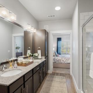 A modern bathroom with a double sink vanity, large mirror, and glass-enclosed shower.