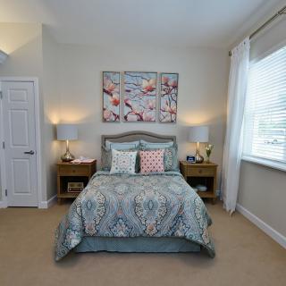 A cozy bedroom with a neatly made bed, colorful artwork above, and natural light streaming in through the window.