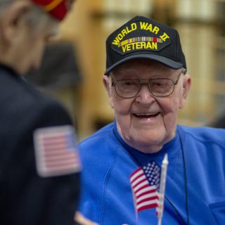 An elderly World War II veteran wearing a hat and holding a small American flag.