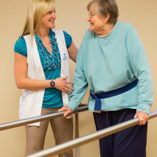 A healthcare professional provides support and assistance to an elderly woman during a rehabilitation session.