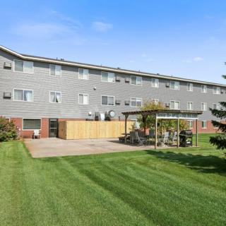 A residential apartment building with a spacious backyard featuring a well-maintained lawn, patio area, and gazebo.