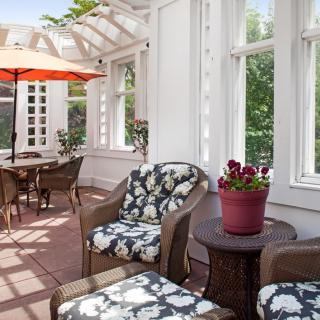 A sunlit patio featuring comfortable seating with floral cushions, a table set, and an umbrella for shade.